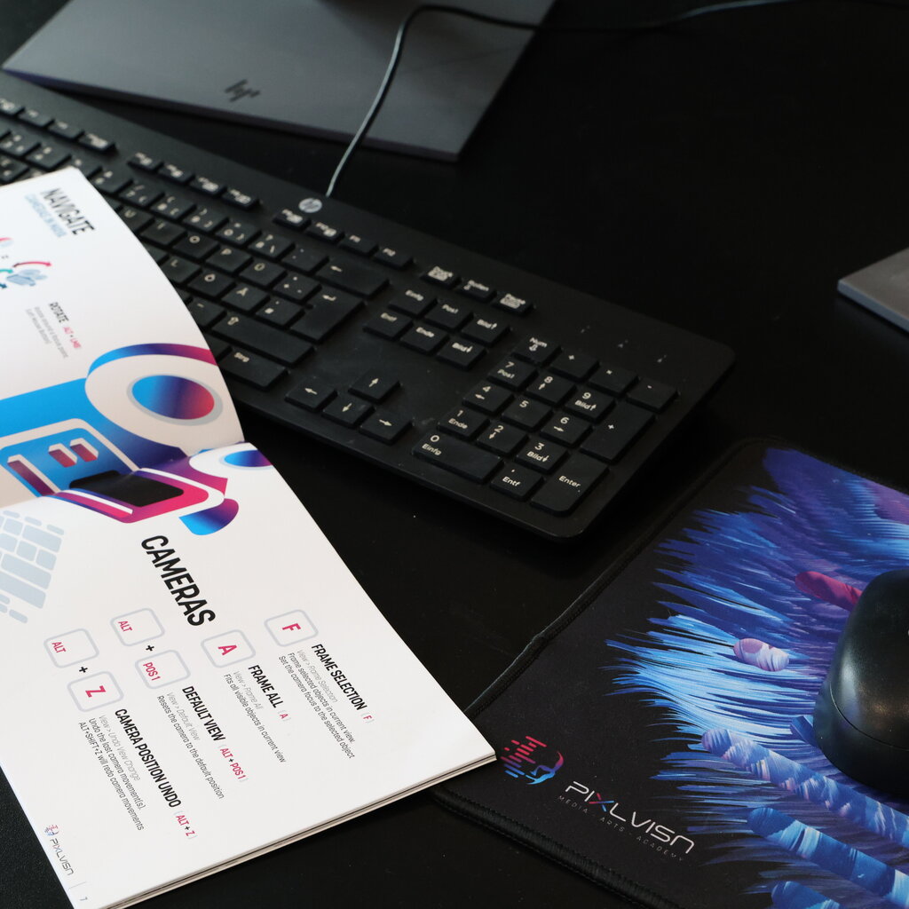 Close-up of a workspace featuring an HP keyboard, PIXL VISN mousepad, mouse, and an open booklet displaying colorful camera navigation tips.